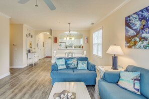 A living room with a blue sofa, a coffee table, and a kitchen in the background. - Golf & Relax! Resort-style Condo in Myrtle Beach (North Myrtle Beach)