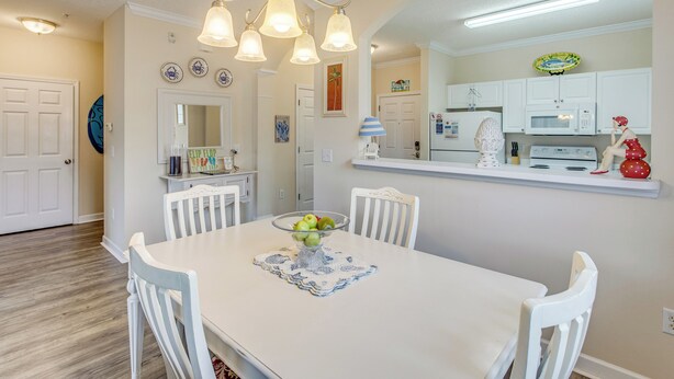 A dining area with a white table, chairs, and a bowl of fruit. There is a kitchen area with white cabinets and a microwave. - Golf & Relax! Resort-style Condo in Myrtle Beach (North Myrtle Beach)