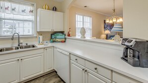 A kitchen with white cabinetry, a built-in dishwasher, a coffee maker, and a window with blinds. - Golf & Relax! Resort-style Condo in Myrtle Beach (North Myrtle Beach)