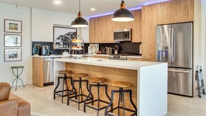 A modern kitchen with a central island, bar stools, stainless steel appliances, wooden cabinets, and pendant lighting. - Fun w/ Friends! Old Town Escape w/ Outdoor Oasis (Scottsdale)