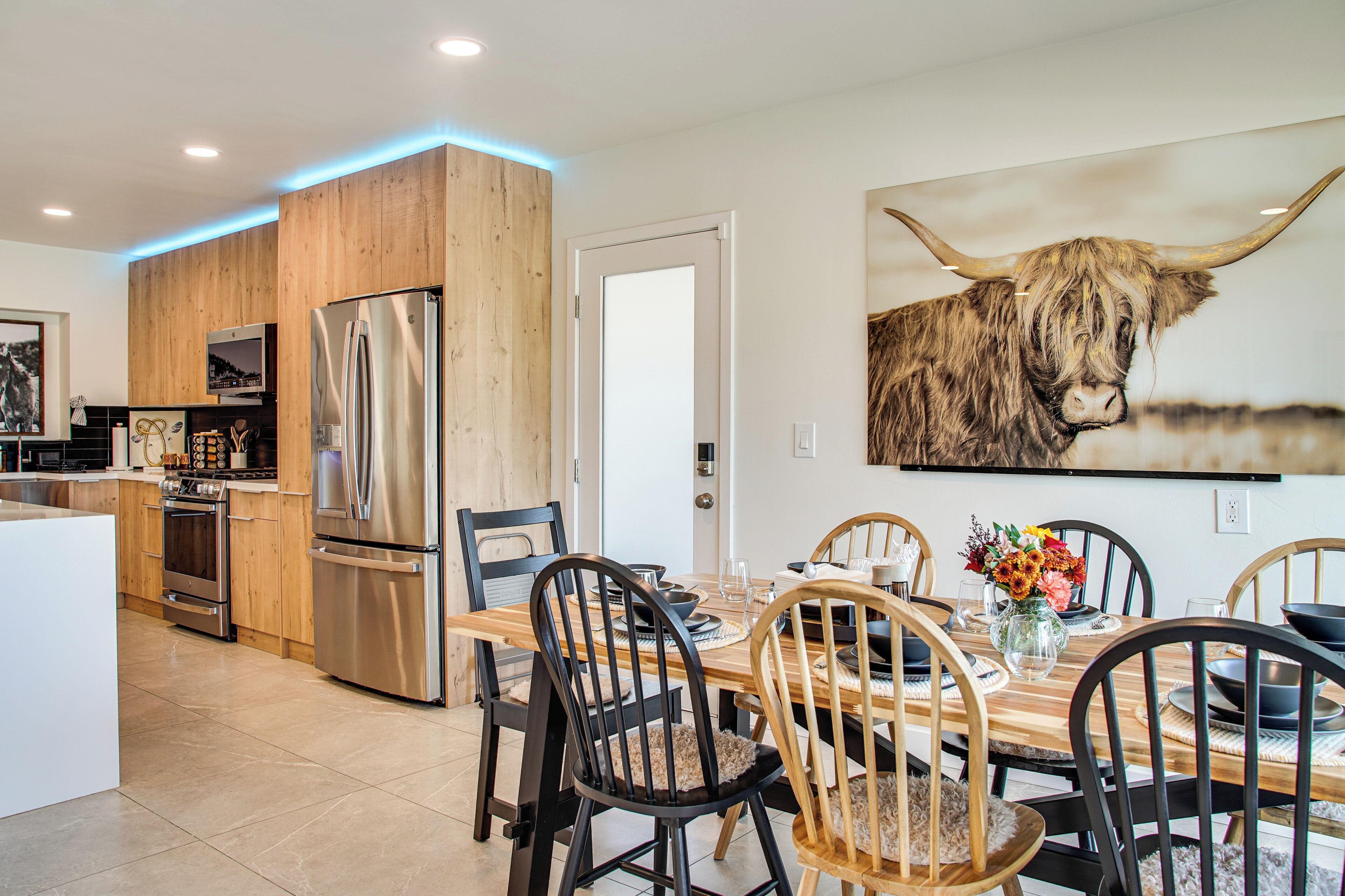 A modern kitchen with wooden cabinetry, stainless steel appliances, and a dining area with a wooden table and chairs.