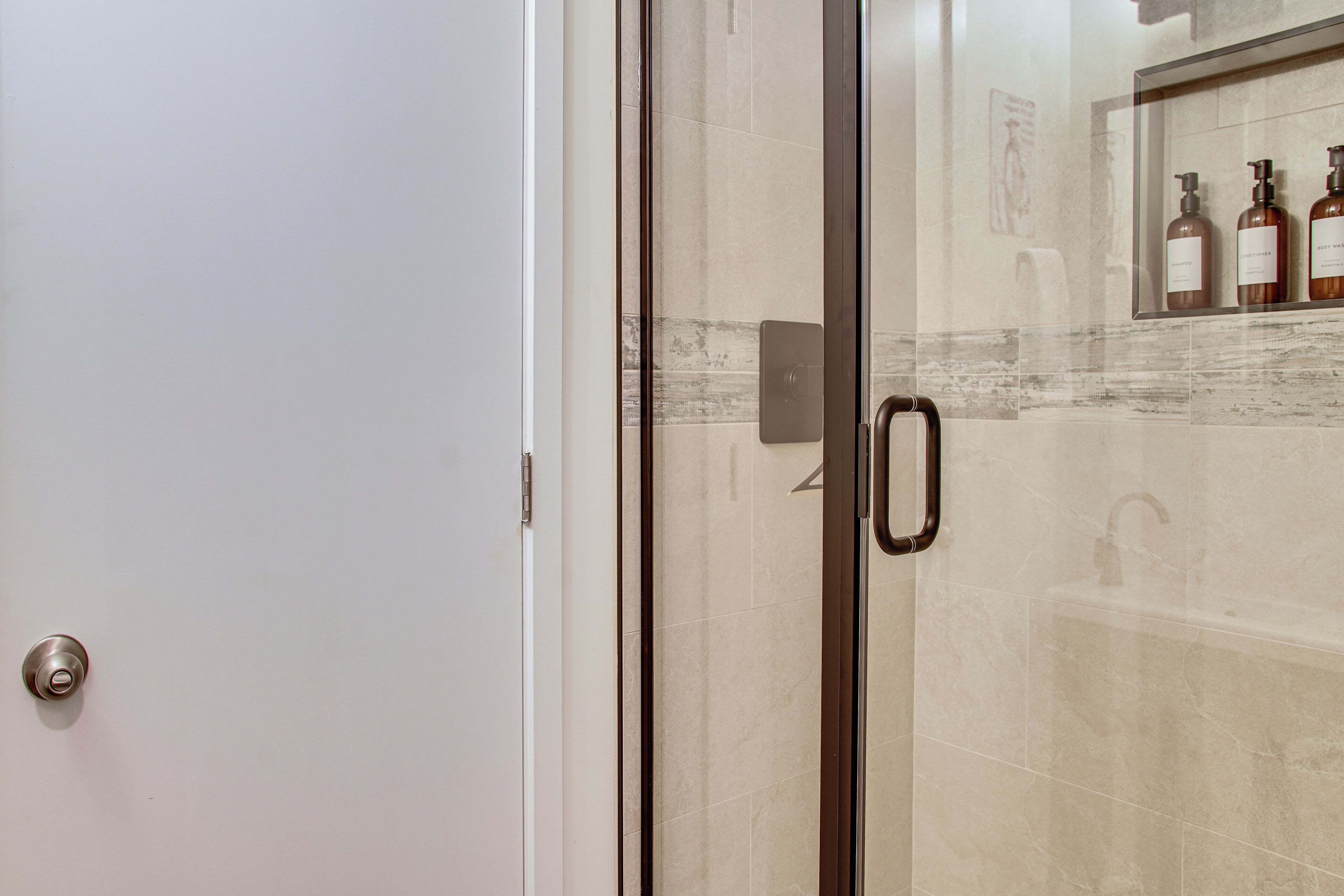 A bathroom with a glass shower door, a handrail, and a shelf with toiletries.
