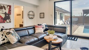 A modern living room with a black leather sofa, a round wooden coffee table, and a large glass sliding door leading to an outdoor patio. - Fun w/ Friends! Old Town Escape w/ Outdoor Oasis (Scottsdale)