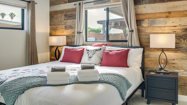 A neatly made bed with a floral bedspread, red and white pillows, and a bedside lamp. - Fun w/ Friends! Old Town Escape w/ Outdoor Oasis (Scottsdale)