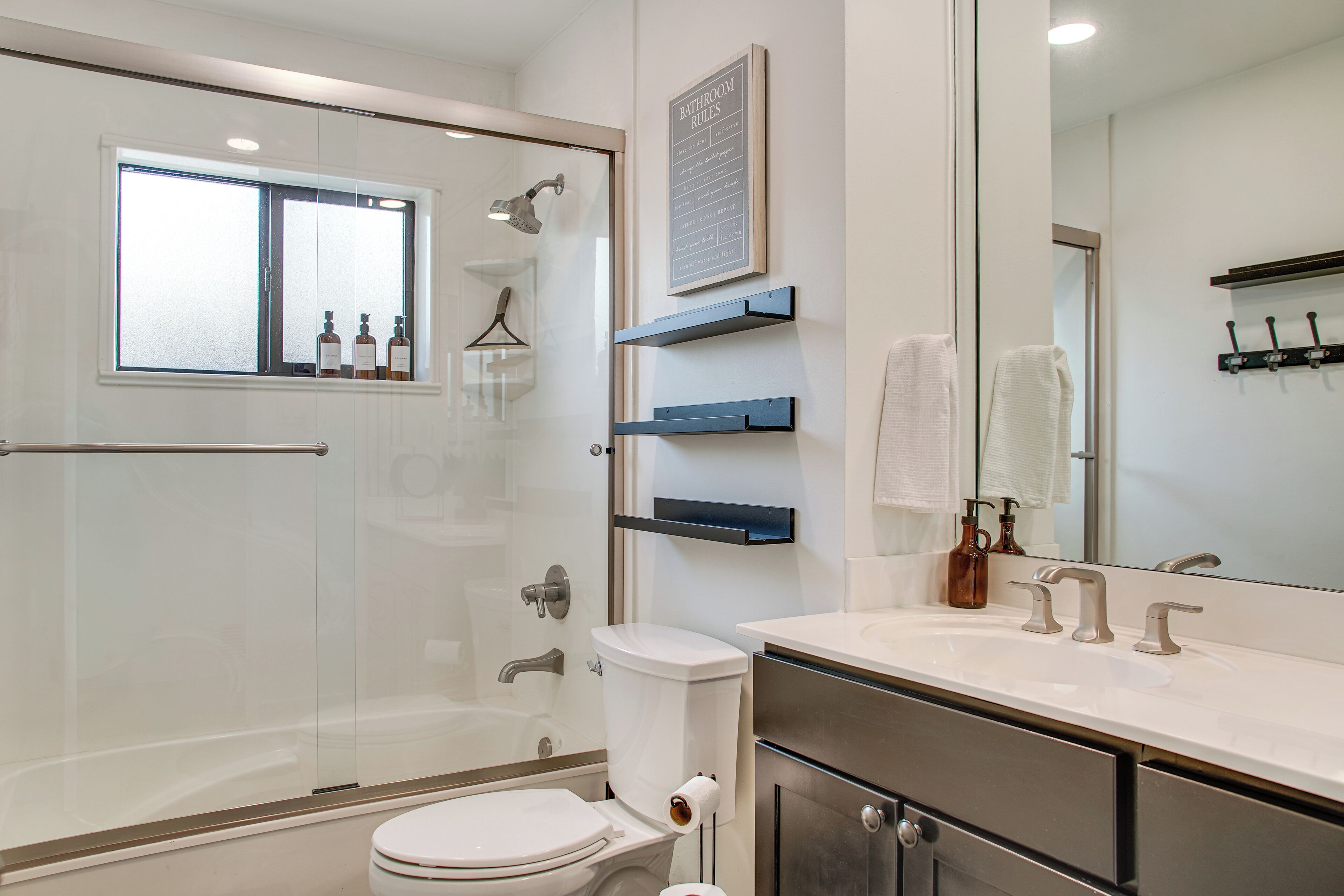 A modern bathroom with a glass shower enclosure, a toilet, a sink with a mirror, and a towel rack.