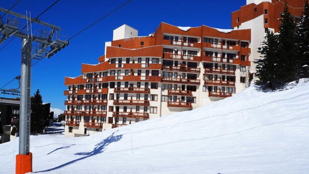 Hotel de diverses plantes amb balcons, situat en una zona nevada amb un teleàs­tic al fons.