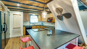 Een moderne keuken met een centraal eiland, houten balken in het plafond, een plafondventilator en een bord aan de muur.
