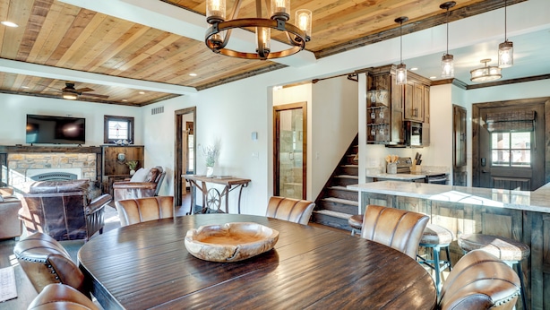 A spacious dining area with a large wooden table and leather chairs, a chandelier, and a stone fireplace.