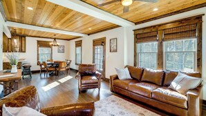A spacious living room with a wooden ceiling, leather furniture, and large windows.
