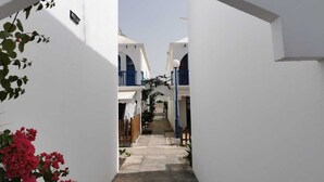 A narrow alleyway with white buildings, blue balconies, and a clear sky.