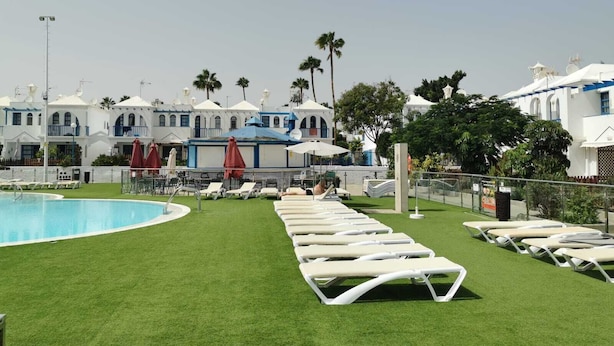 A poolside area with artificial grass, sun loungers, and umbrellas.