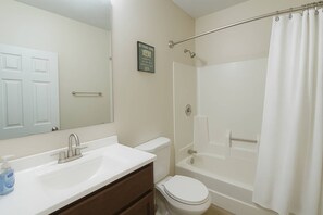 A bathroom with a white sink, mirror, toilet, and bathtub.