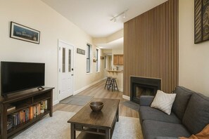 A living room with a TV, bookshelf, coffee table, sofa, and fireplace. - Pet-Friendly Soulard Townhouse · 2BR/2BA · Parking + Rooftop Deck (St. Louis)