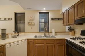 A kitchen with wooden cabinets, a stainless steel sink, a coffee bar sign, and a coffee maker.