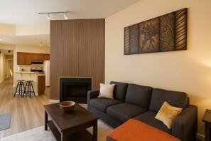 A modern living room with a sofa, a coffee table, a fireplace, and a kitchen in the background.