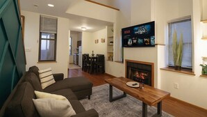 Ein Wohnzimmer mit einer Couch, einem Couchtisch, einem Kamin und einem an der Wand montierten Fernseher, der Filmplakate zeigt.