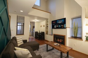 A living room with a sofa, a coffee table, a fireplace, and a TV mounted on the wall displaying movie posters. - Soulard River-View Loft - 2 King BR - Parking (St. Louis)