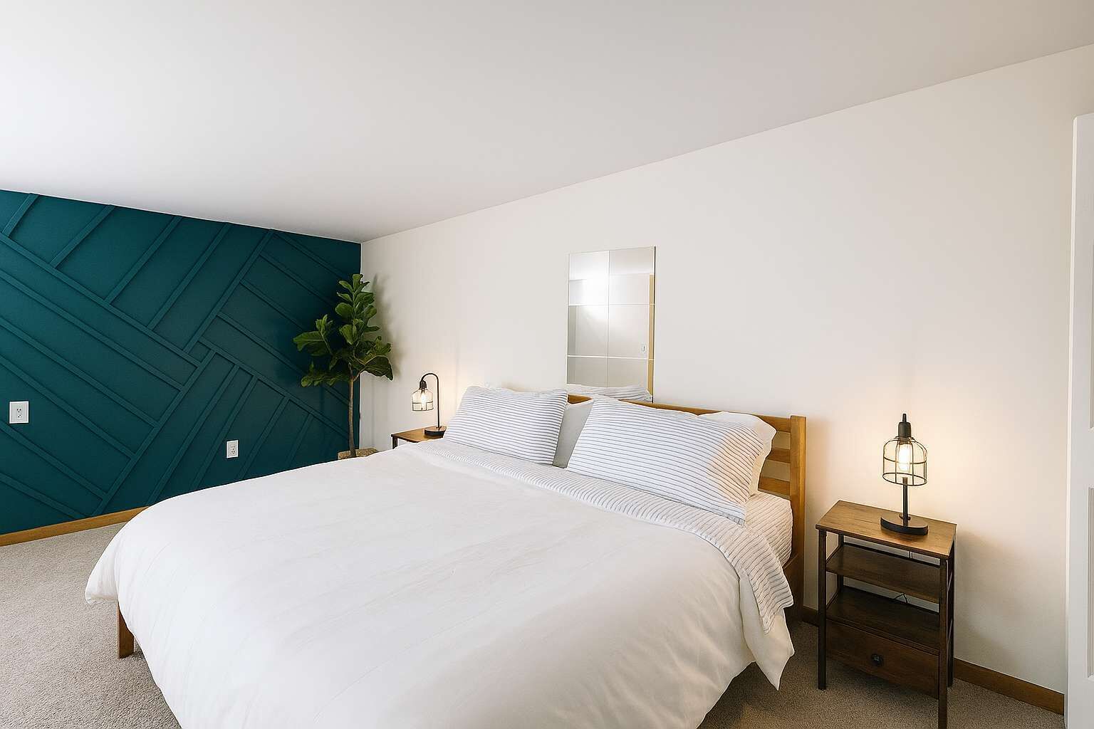 A bedroom with a large bed, a nightstand, a wall-mounted mirror, and a teal accent wall.