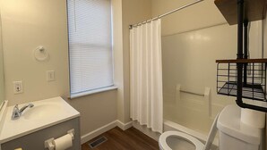 Une salle de bain équipée de toilettes, d’un lavabo, d’une douche et d’une fenêtre avec des stores.