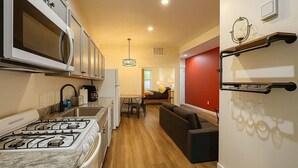 Une cuisine compacte équipée d’une cuisinière à gaz, d’un four à micro-ondes et d’un évier. On y trouve également un coin repas avec une table et des chaises, ainsi qu’un mur d’accent de couleur rouge.