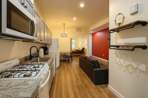 Une cuisine compacte équipée d’une cuisinière à gaz, d’un four à micro-ondes et d’un évier. On y trouve également un coin repas avec une table et des chaises, ainsi qu’un mur d’accent de couleur rouge.