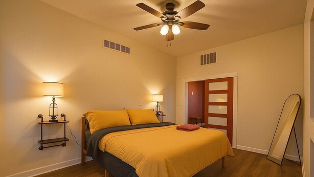 Une chambre à coucher avec un lit, deux lampes de chevet, un ventilateur de plafond et un plancher en bois.