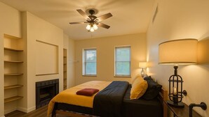 Une chambre à coucher avec un lit, un ventilateur de plafond, une lampe et une cheminée.