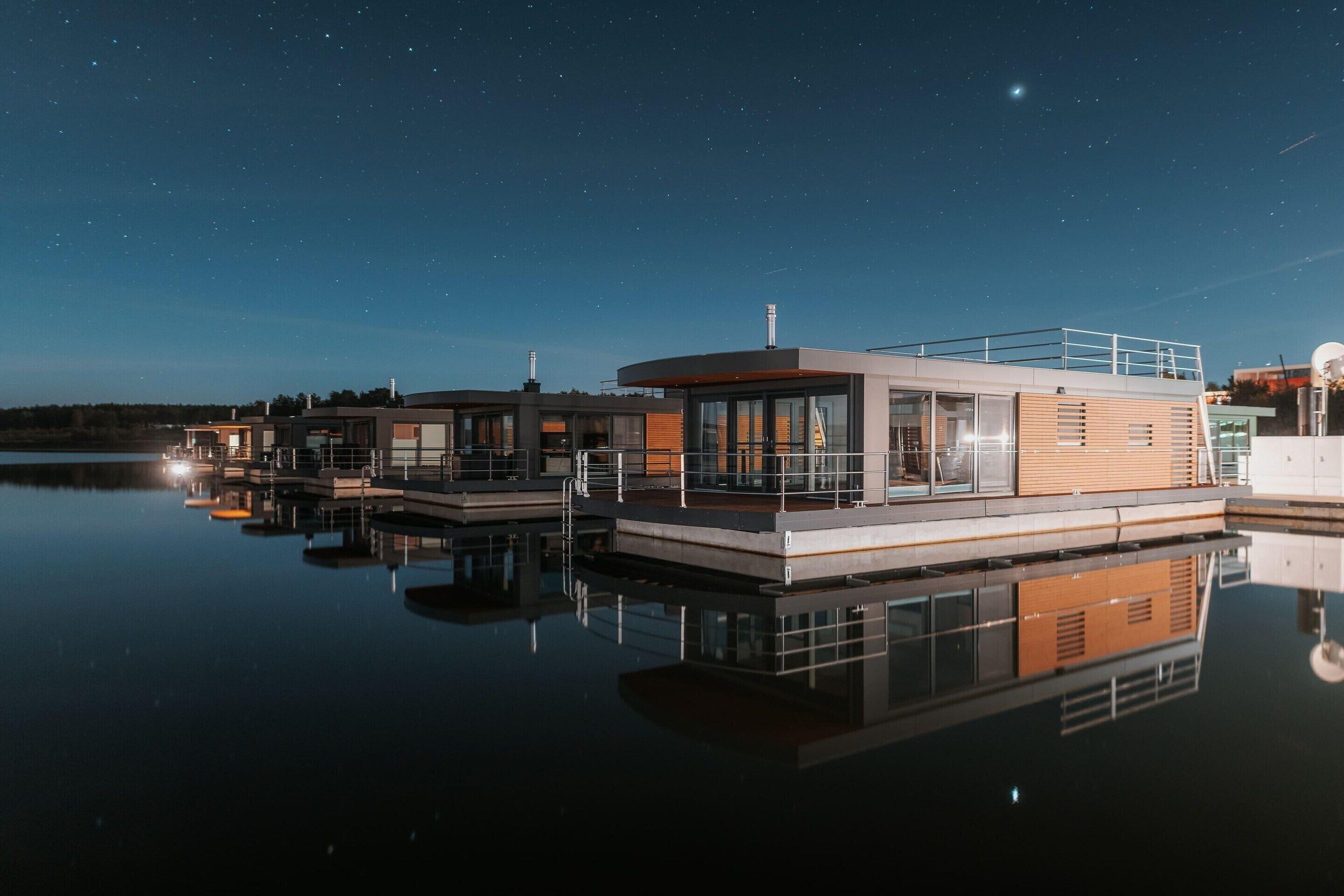 Een pand aan het water met moderne architectuur, bestaande uit meerdere gebouwen met grote ramen en een spiegelend wateroppervlak.