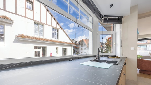 A modern kitchen with a large window, a black countertop, and a sink. - Holiday Home in Middelkerke Near Beach (Middelkerke)