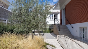 A modern house with a white exterior and a red accent wall, a staircase leading to the upper floor, and a garden area with a wicker chair and a table. - Holiday Home in Middelkerke Near Beach (Middelkerke)