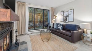 Ein modernes Wohnzimmer mit Kamin, einer Couch, einem Couchtisch und einer großen Schiebeglastür, die auf einen Balkon führt.