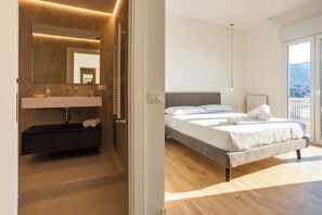 A modern bedroom with a large bed, a built-in bench with towels, a bedside table, and a view of the outdoors. - Luxury Cefalù S.Mary (Cefalù)
