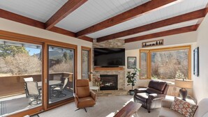 A spacious living room with a stone fireplace, leather furniture, and large windows offering a view of the outdoors. - Cozy Keystone Townhome Near Slopes, Poolhouse with Sauna & Hot Tub (Keystone)