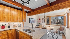 A modern kitchen with wooden cabinets, a granite countertop, and a dining area with a table and chairs. - Cozy Keystone Townhome Near Slopes, Poolhouse with Sauna & Hot Tub (Keystone)