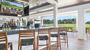 Een bar met een televisiescherm, houten stoelen en uitzicht op een golfbaan.
