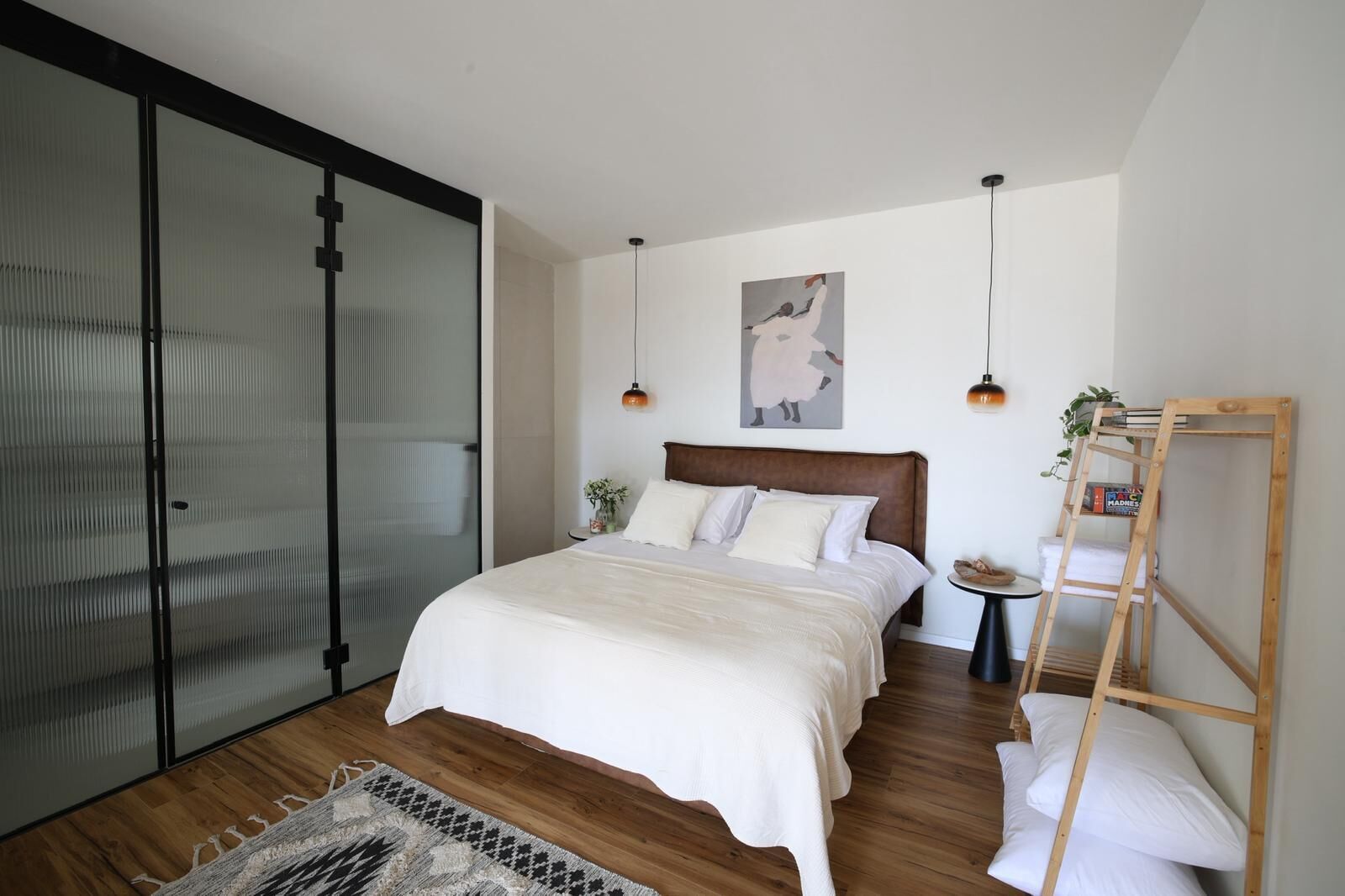 A bedroom with a large bed, a wooden ladder, a small table with a plant, and a sliding door.