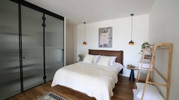 A bedroom with a large bed, a wooden ladder, a small table with a plant, and a sliding door.