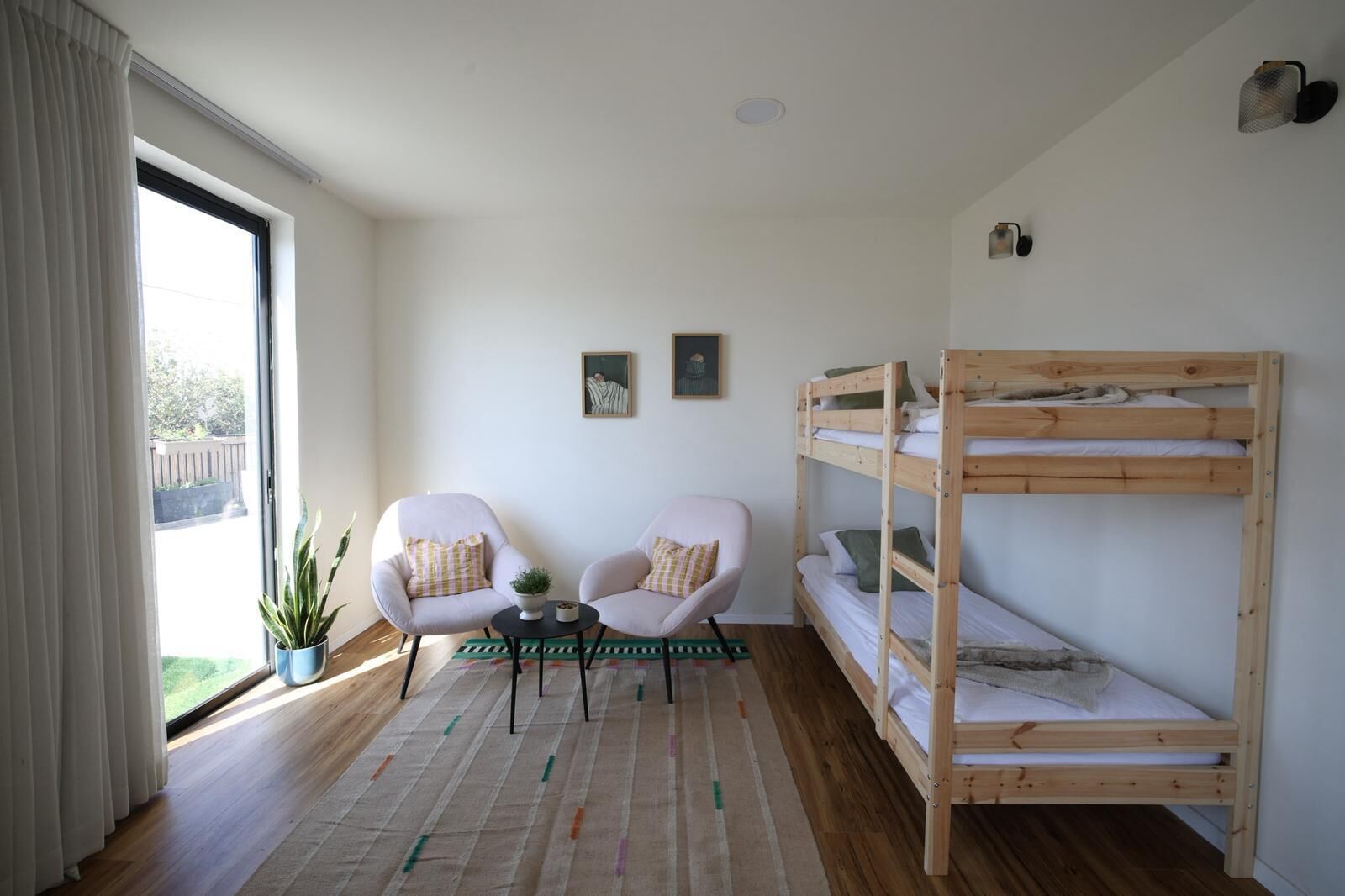 Ein Zimmer mit einem Etagenbett, zwei Sesseln, einem kleinen Tisch und einem Blumentopf.