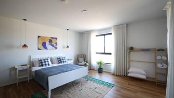 Une chambre moderne avec un lit, des tables de chevet, une fenêtre avec des rideaux, une plante en pot et une étagère avec des serviettes.