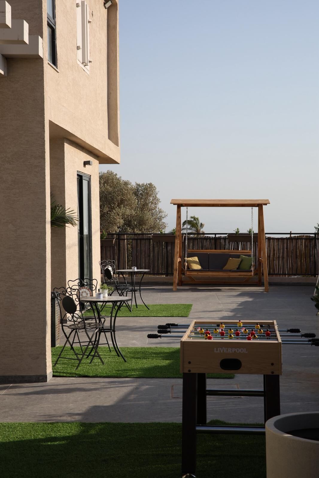An outdoor patio area with a foosball table, a wooden swing set, and a seating area with cushions.