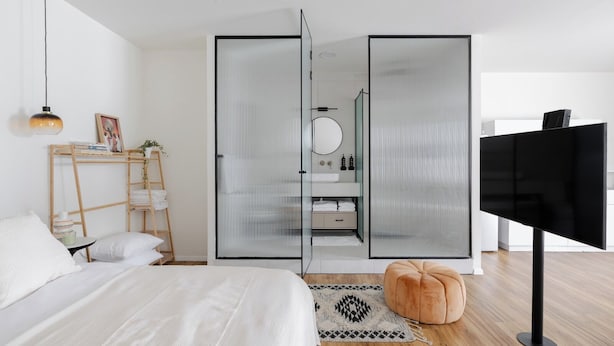 Une chambre à coucher moderne, avec un lit, une télévision, une armoire avec un miroir et un petit tabouret.