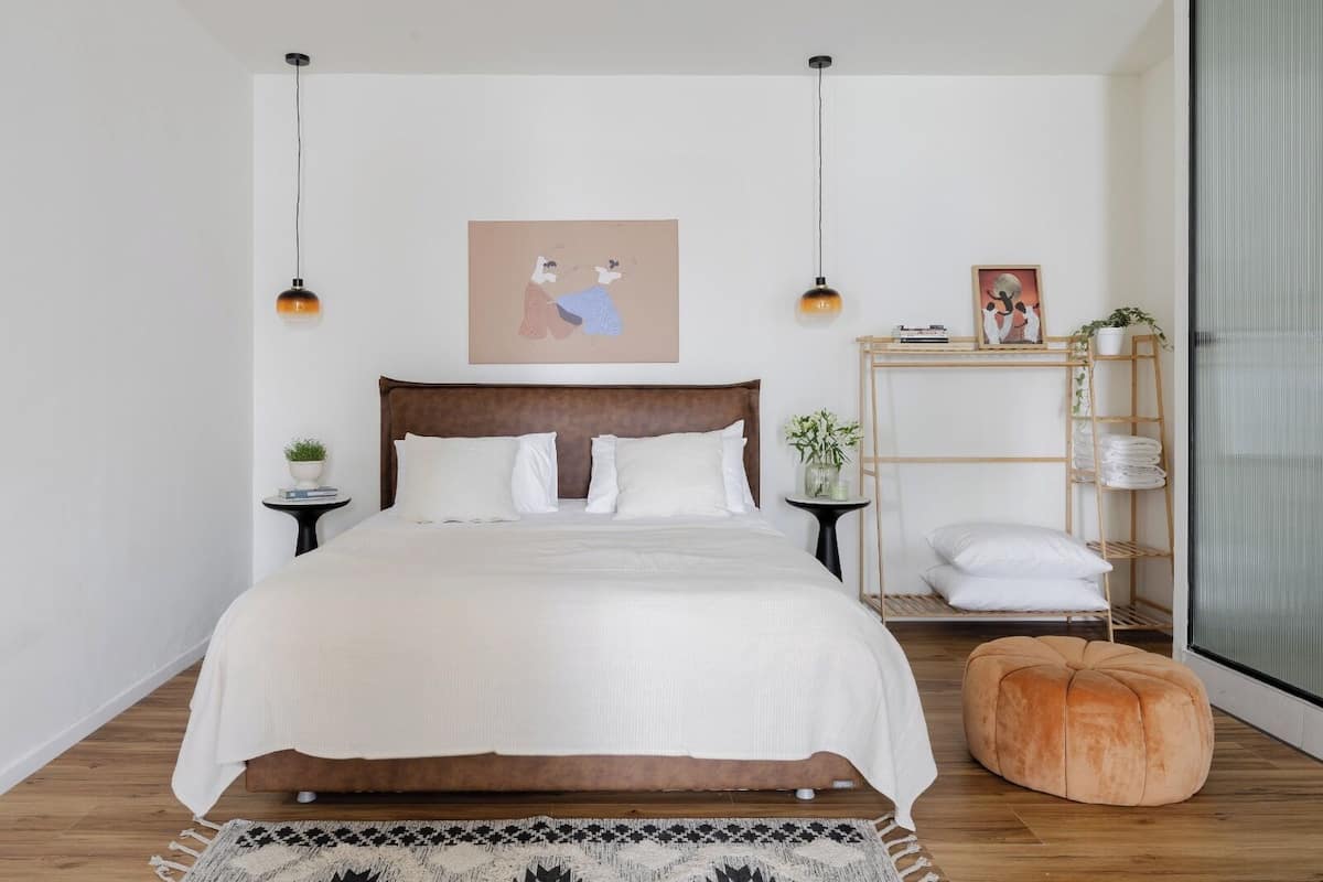 Ein ordentlich eingerichtetes Schlafzimmer mit einem großen Bett, Nachttischen, einer hölzernen Bank, einem Regal mit gefalteten Handtüchern und einer Pendelleuchte.