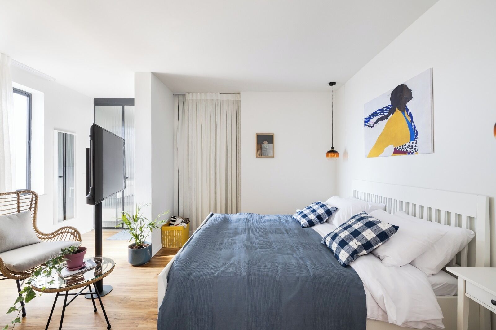 Une chambre à coucher moderne avec un grand lit, un téléviseur à écran plat, un fauteuil, une petite table avec une plante et un tableau accroché au mur.
