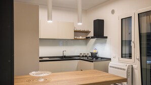 A modern kitchen with a wooden table, white cabinets, a black countertop, and a built-in oven. - Luxury Apartment Cefalù Giglio (Cefalù)