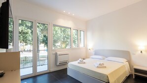 A modern bedroom with a large bed, a desk, and a balcony with a view of trees. - Luxury Apartment Cefalù Giglio (Cefalù)