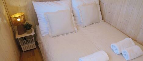 A neatly made bed with white linens and pillows, a bedside lamp, and two rolled towels on the floor.
