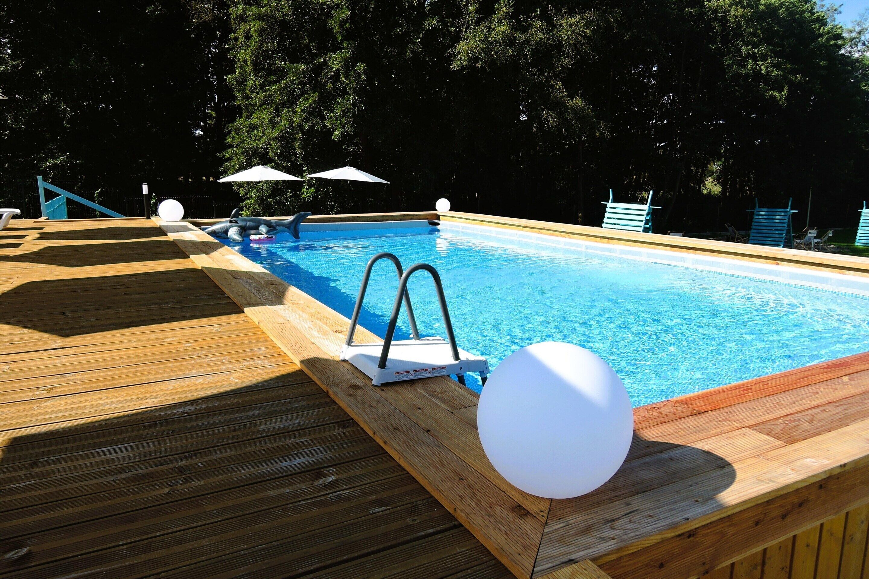 A wooden deck with a swimming pool, two umbrellas, and a lifeguard stand.