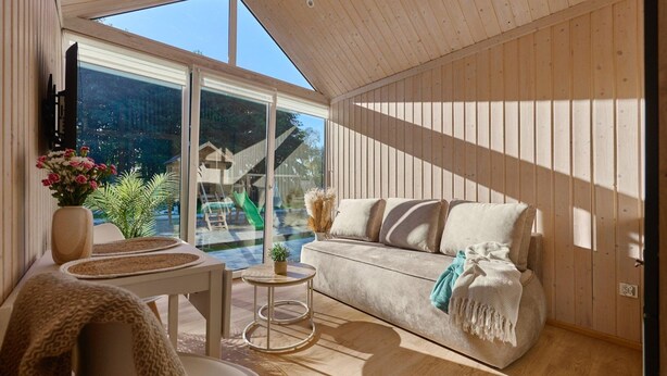 A modern interior with a wooden ceiling, a sofa, a small round table, and a view of a swimming pool and outdoor area. - Holiday Homes With Swimming Pool, Close to the sea (Międzyzdroje)
