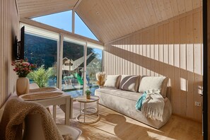 Um interior moderno com teto de madeira, um sofá, uma pequena mesa redonda e vista para uma piscina e área externa.