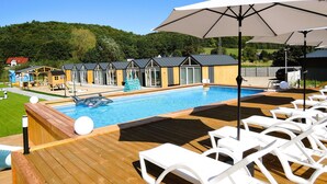 A pool area with lounge chairs and umbrellas, surrounded by wooden deck and a pool. - Holiday Homes With Swimming Pool, Close to the sea (Międzyzdroje)